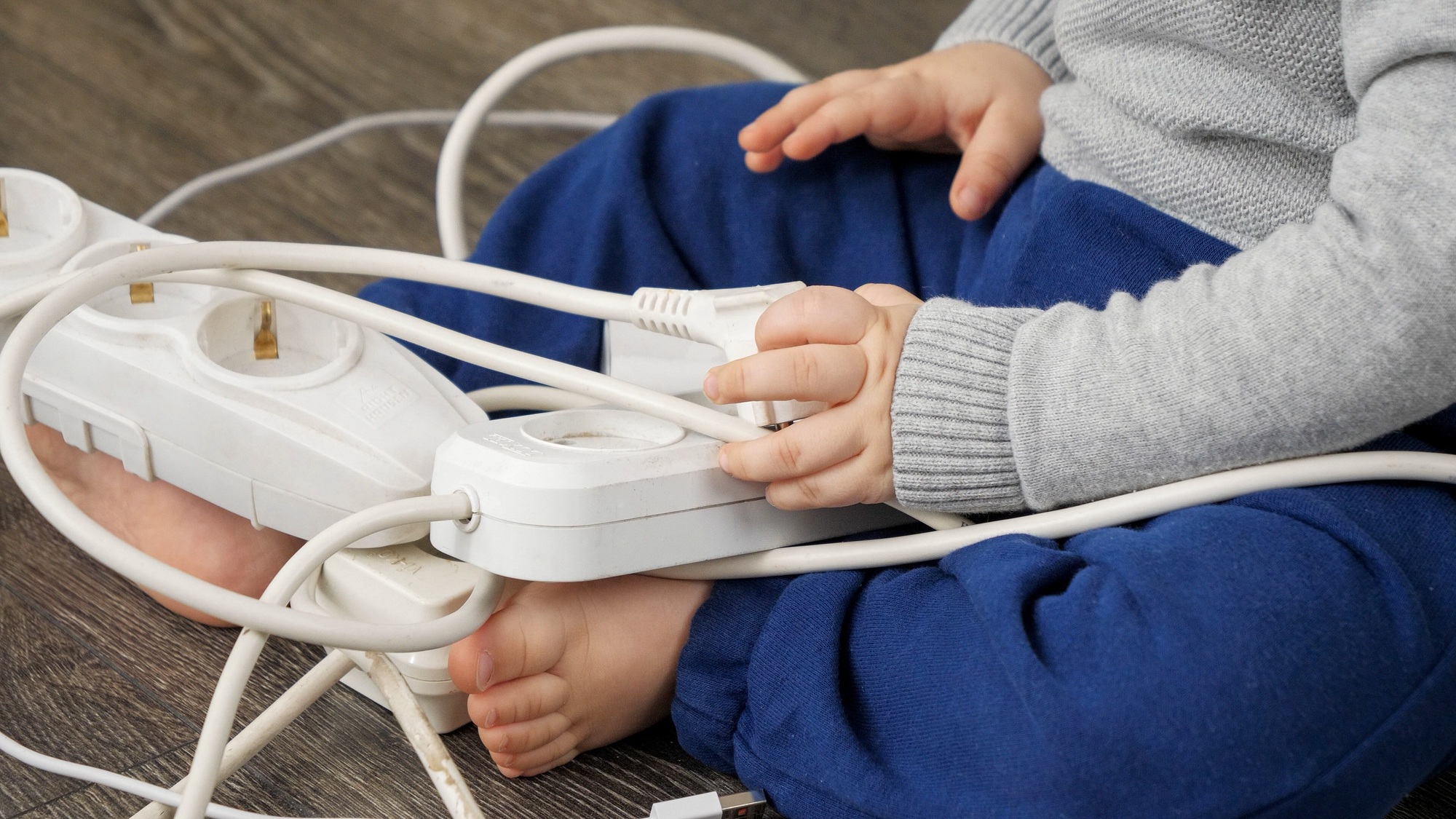 Closeup of little baby boy inserting electric plug. CHild playing with wires and cables.